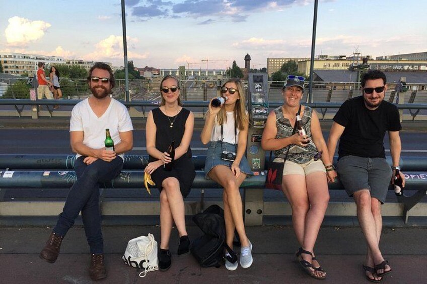 Eine Gruppe von Personen sitzt auf einer Bank, im Hintergrund eine Stadtansicht. 3