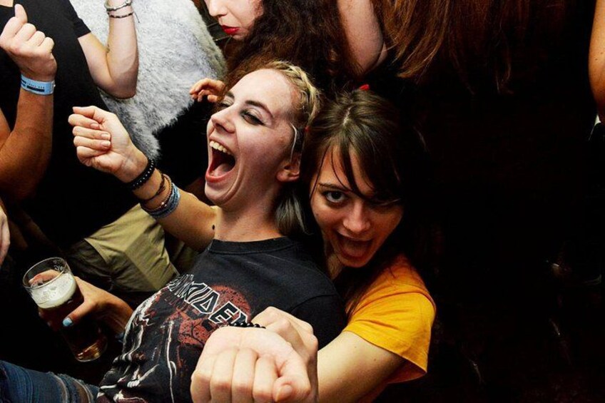 Une personne portant un t-shirt à motifs, tenant une boisson et entourée d’autres personnes dans un cadre social. 2