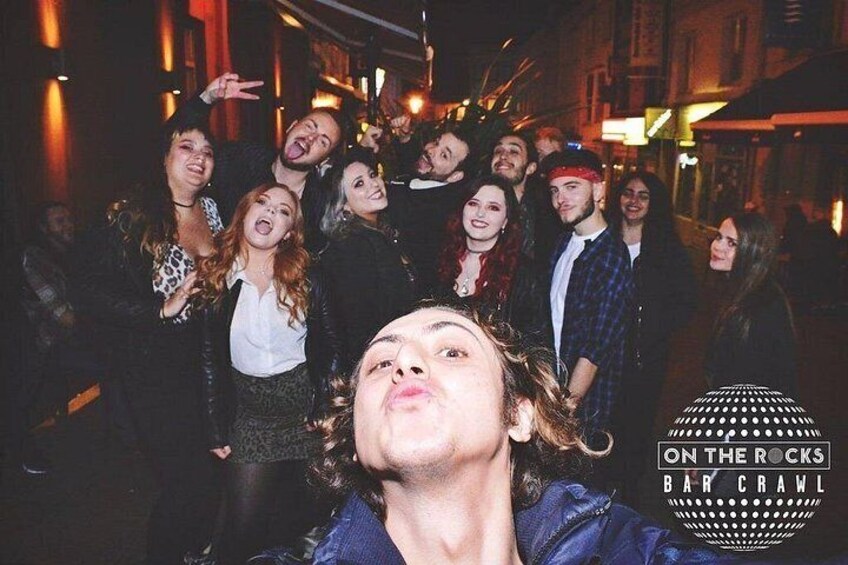 Un groupe de personnes lors d’un événement en plein air, peut-être un concert ou un festival, avec un logo sur lequel on peut lire : « ON THE ROCKS BAR CRAWL ». 4