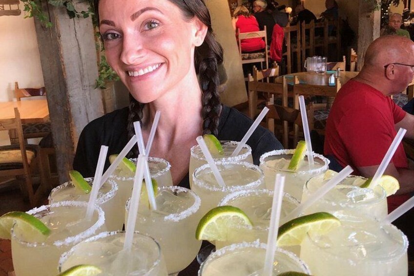 A person holding several margaritas with lime garnishes and straws. 1