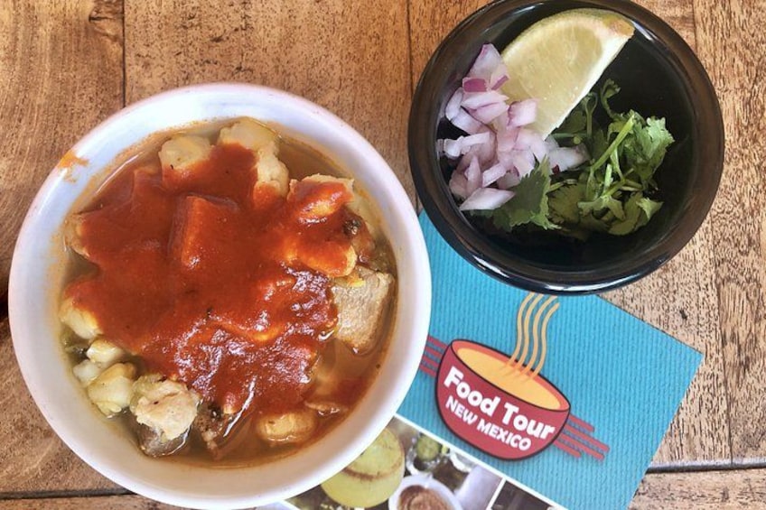 A bowl of soup with a slice of lime and chopped onions on the side, and a menu with a Food Tour New Mexico logo. 2