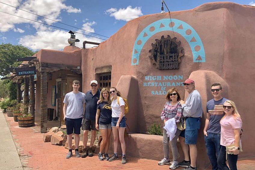 A group of people standing in front of a building with a sign that reads 'HIGH NOON RESTAURANT & SALOON.' 3