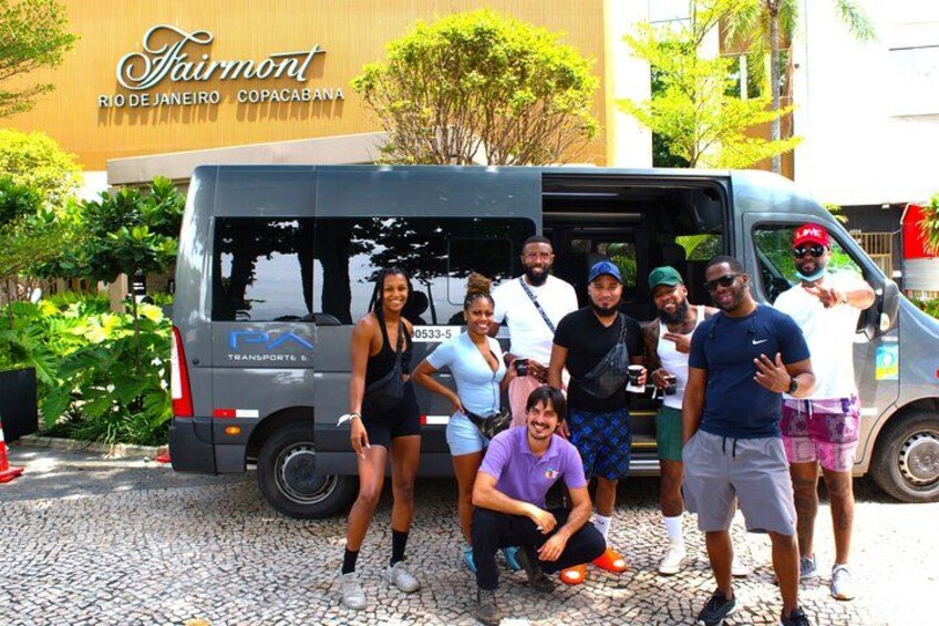 A group of people posing in front of a van with 'Fairmont Rio de Janeiro Copacabana' written on the building behind them. 4