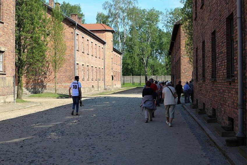 A cobblestone street lined with brick buildings, a person in a white shirt and shorts walking, and a group of people standing near the buildings. 3