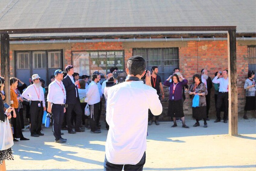 A group of people standing in front of a brick building, some taking photos. 1