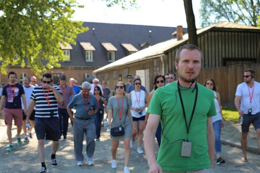 A group of people walking outdoors, some wearing lanyards, with buildings and trees in the background. 2