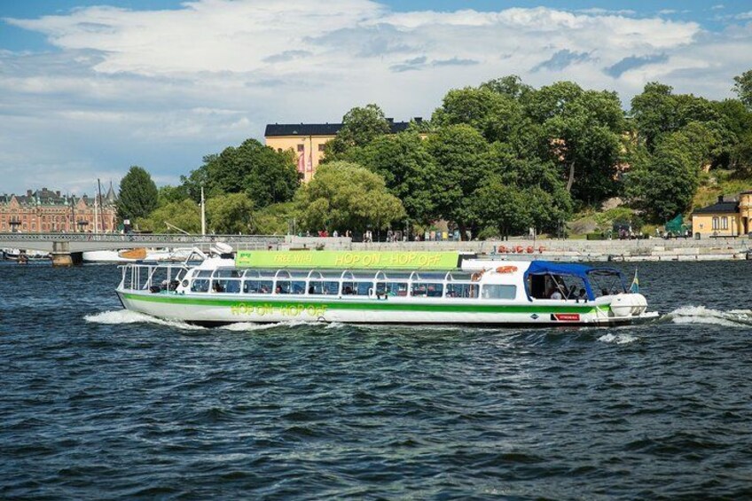 Un bateau de croisière fluviale aux couleurs verte et blanche, naviguant sur une rivière avec un pont et des bâtiments en arrière-plan. 1