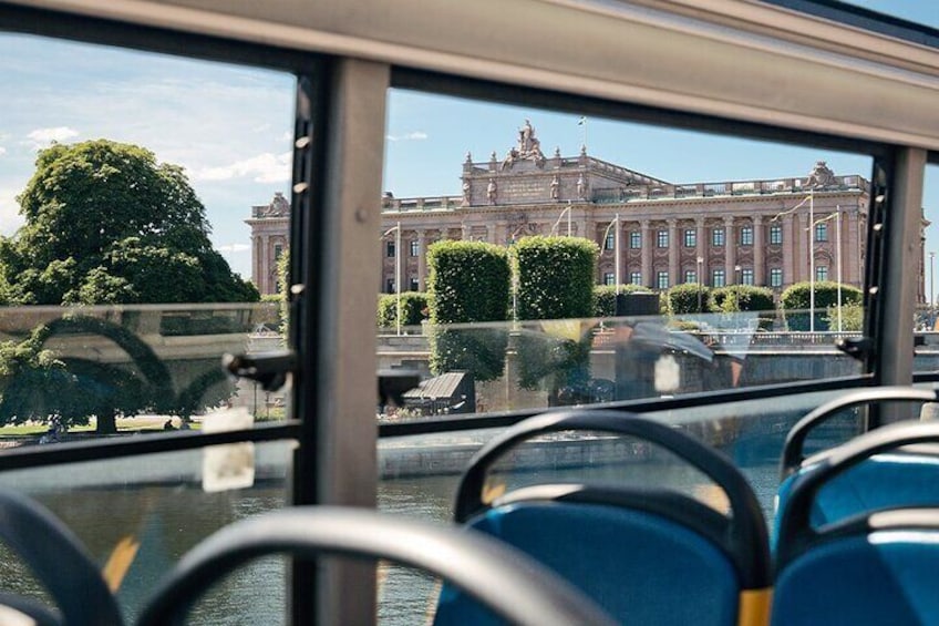 L'intérieur d'un autobus avec des sièges bleus et une vue sur un grand bâtiment historique surmonté d'un drapeau. 3