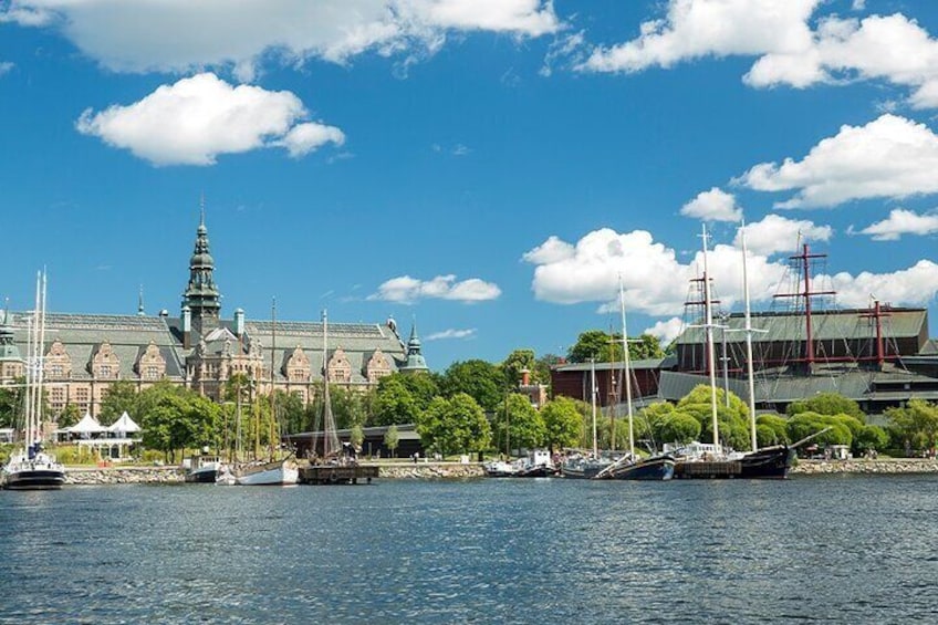 Un bâtiment historique doté d’un toit végétalisé et d’une tour, entouré d’arbres et bordé par des bateaux sur l’eau. 2