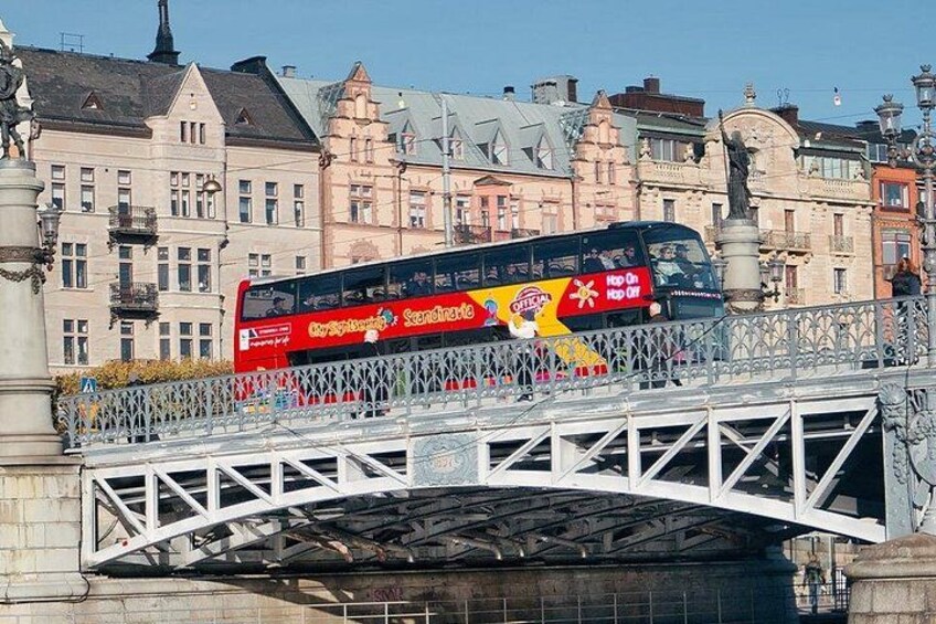 A red double-decker bus on a bridge with historic buildings in the background. 4
