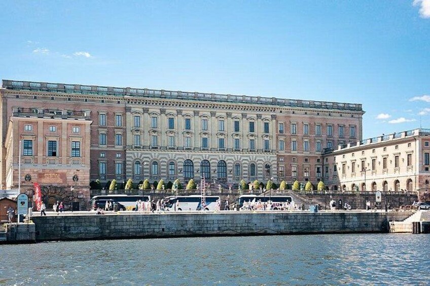 A large historic building with multiple windows and a portico, situated by a body of water with a dock and several boats. 2