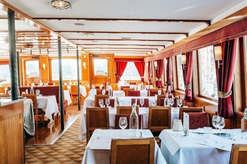 En restaurant med træpaneler, borde dækket med hvide duge og røde gardiner. 2