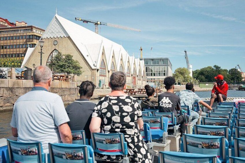 People seated on a boat, a white building with a pointed roof, and a crane in the background. 3