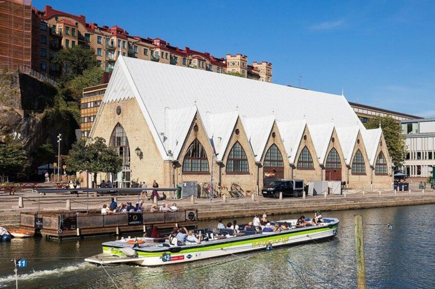 A boat on a river, a building with a white roof, and a cityscape with buildings in the background. 1