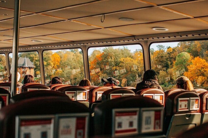 El interior de un autobús con pasajeros sentados, ventanas que muestran follaje otoñal y un edificio visible en el exterior. 5