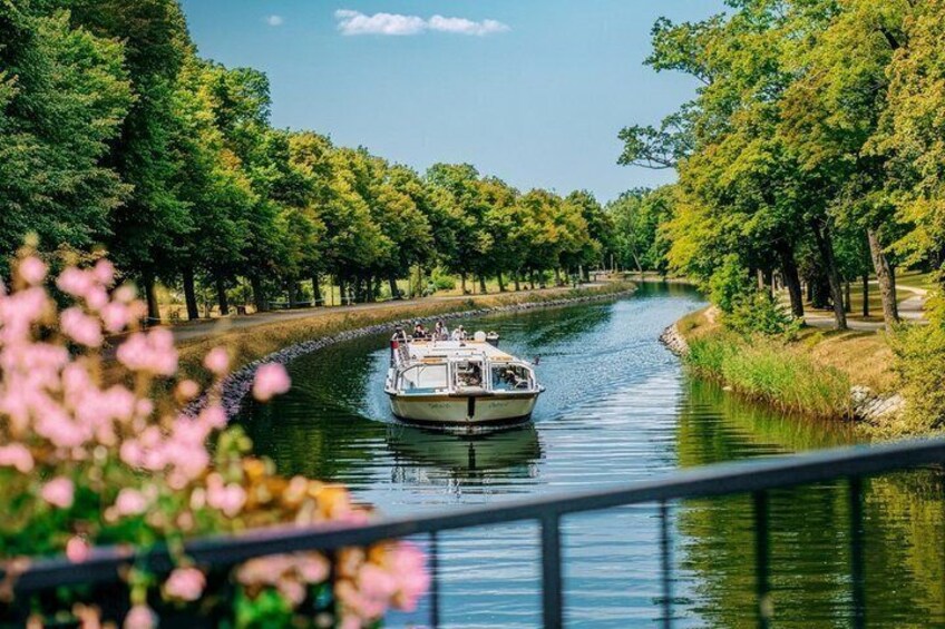Ein schmaler Wasserweg mit einem Boot, umgeben von dichtem Baumbestand und einem klaren Himmel. 1