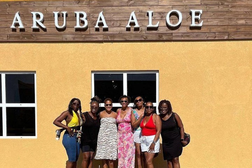 A group of people standing in front of a building with the sign 'ARUBA ALOE'. 2