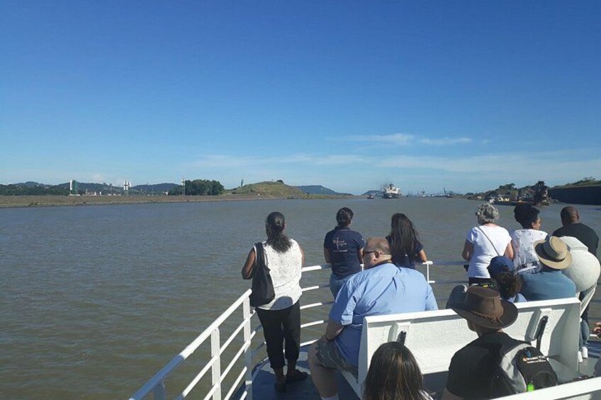 Een groep mensen in een boot, een rustige rivier en schepen in de verte. 2