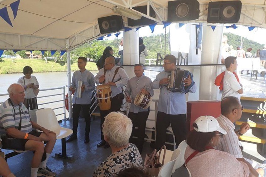 Een groep mensen op een boot, sommigen bespelen instrumenten, onder een tent. 1