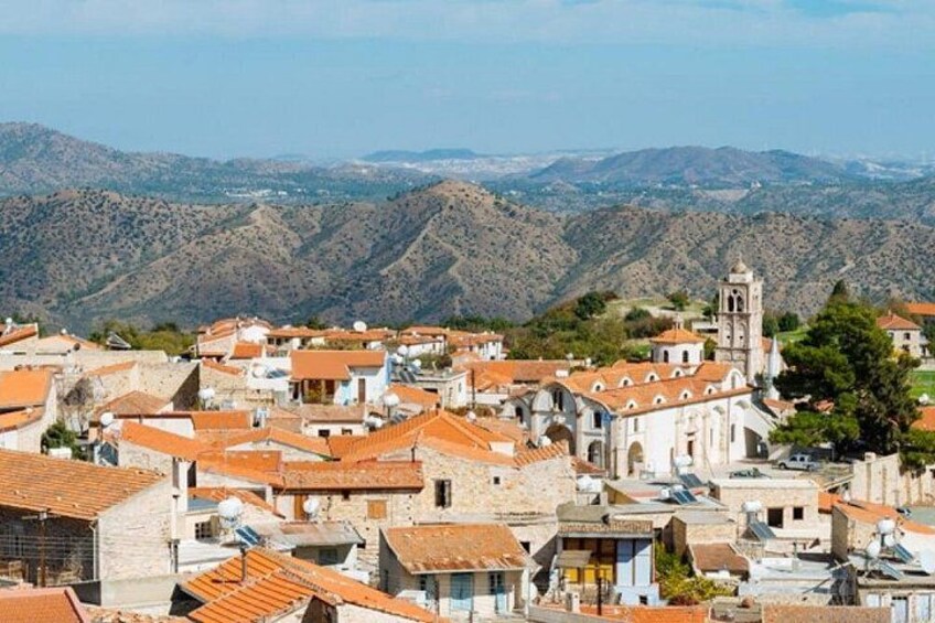 Un pueblo montañoso con edificios de tejados de terracota, una iglesia destacada con un campanario y colinas ondulantes al fondo. 2