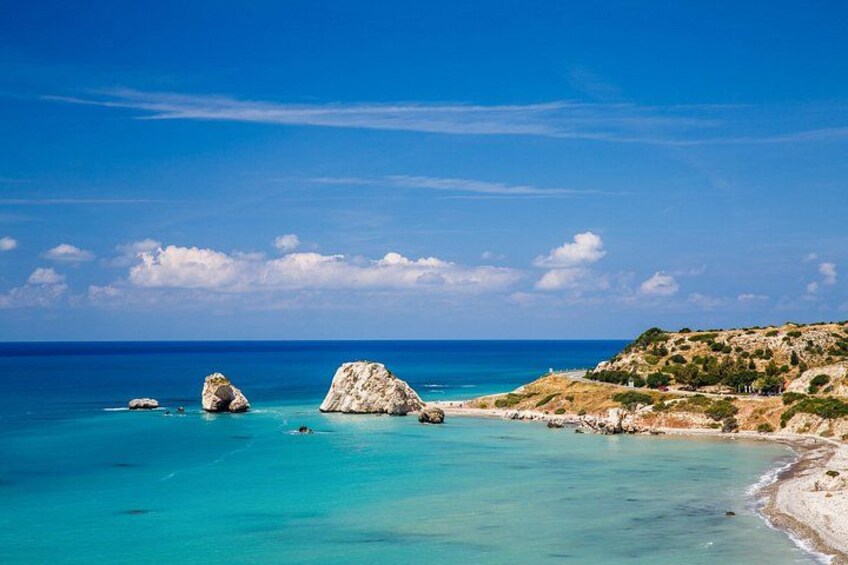 A coastal landscape with clear turquoise waters, rocky outcrops, and a hilly terrain with sparse vegetation. 2