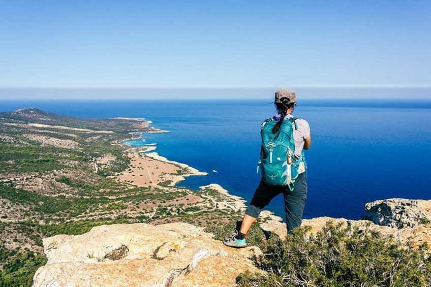 En person vandrar på en bergig utskjutande klippa med utsikt över ett kustlandskap, och har fri sikt över havet och det avlägsna landskapet. 3