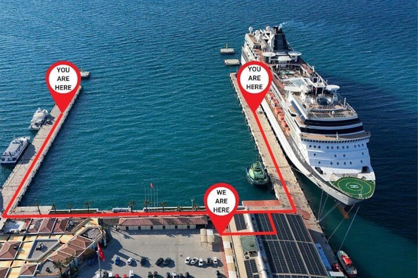 A cruise ship docked at a port with two red location markers indicating 'YOU ARE HERE' and 'WE ARE HERE'. 1