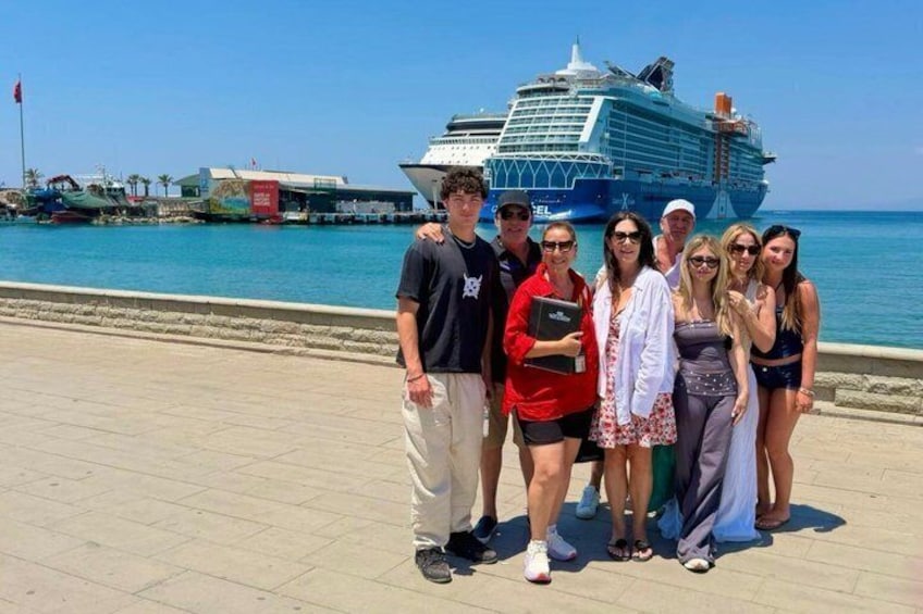 A group of people posing in front of a cruise ship on a sunny day. 4