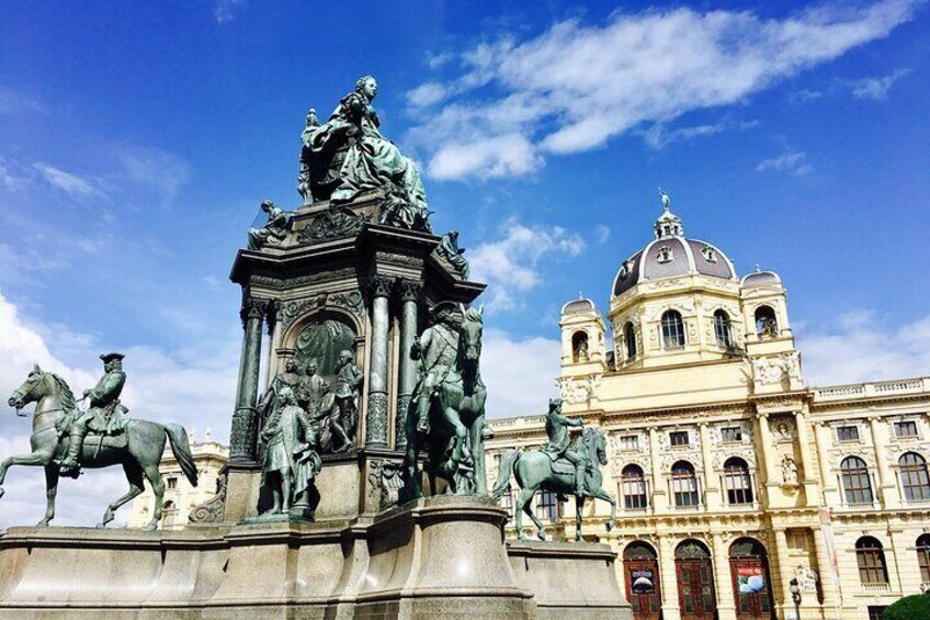A historical monument with equestrian statues and a classical building with a dome in the background. 2