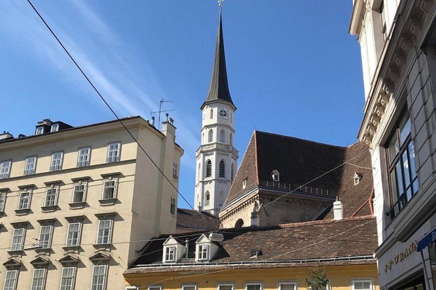 En kirke med et højt spir og et tårn med et ur, omgivet af bygninger med klassisk arkitektur. 4