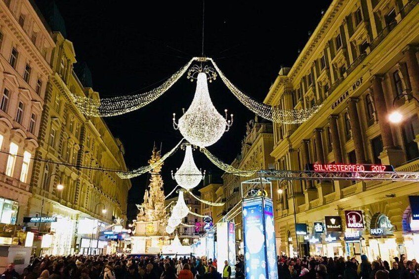 Una plaza concurrida con decoraciones navideñas iluminadas, incluyendo grandes adornos blancos y un árbol dorado. 4