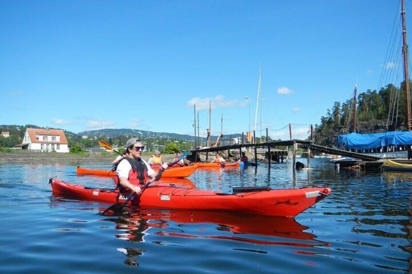 A person in a red kayak on calm water with other kayaks and a dock in the background. 1