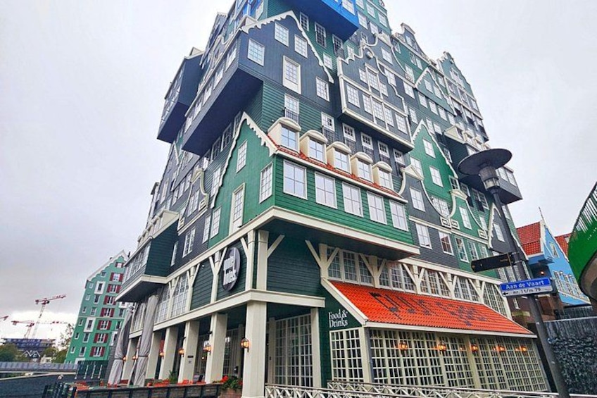 Un immeuble à plusieurs étages, doté d’une façade verdoyante et de bordures blanches, avec une grande horloge et une enseigne indiquant un restaurant. 3