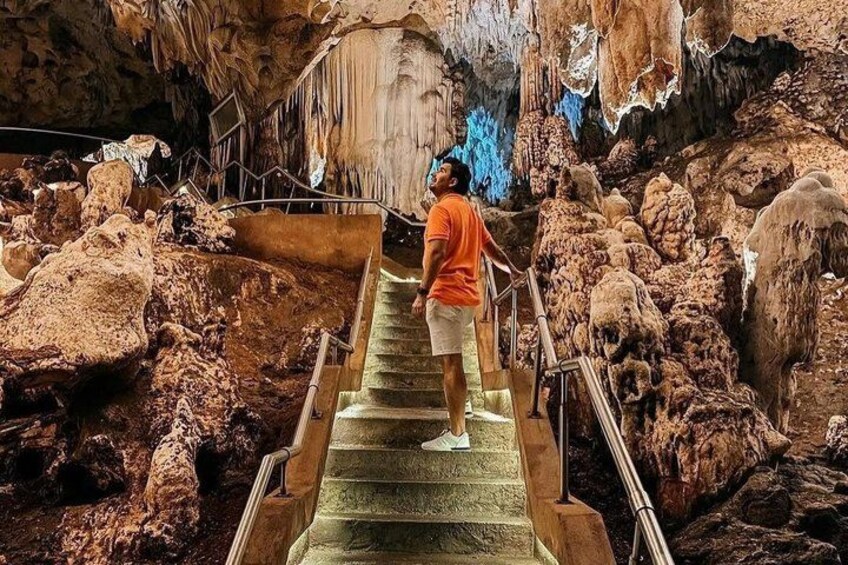 A person standing on a staircase inside a cave with stalactites and stalagmites. 1