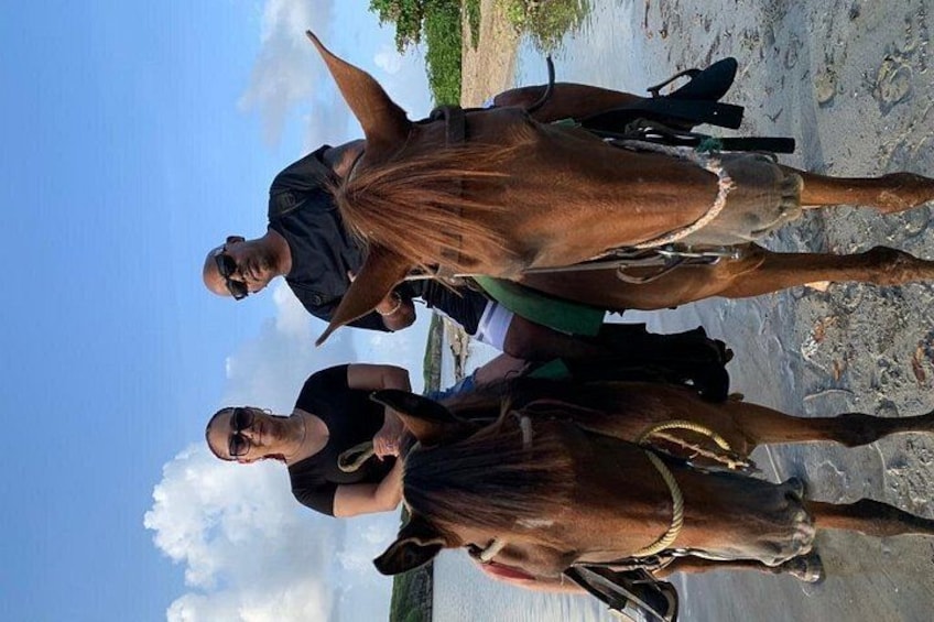 Tres personas están de pie junto a un caballo en una playa con cielo despejado. 2