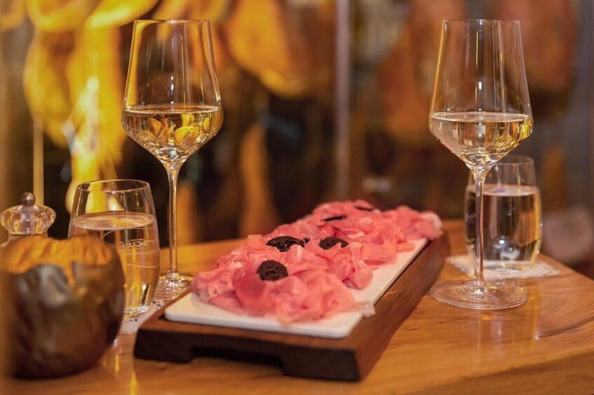 Un tavolo in legno con un piatto di cibo rosa, probabilmente carne, e diversi bicchieri di vino bianco. 4