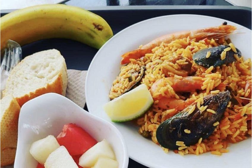 Eine Portion Fischpaella mit Brot und einer Schale Obst. 4