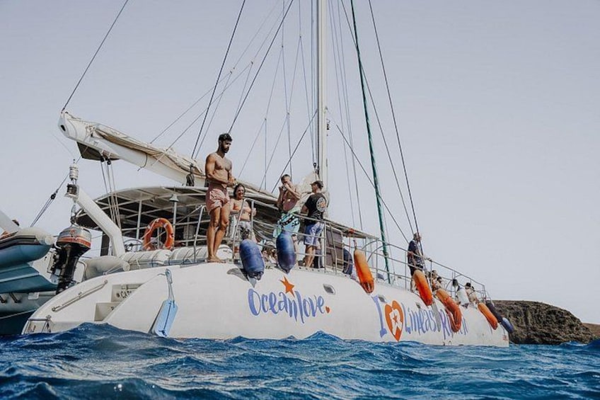 Ein Segelboot mit Personen an Deck, einer Rettungsboje und einem Felsen im Wasser. 3