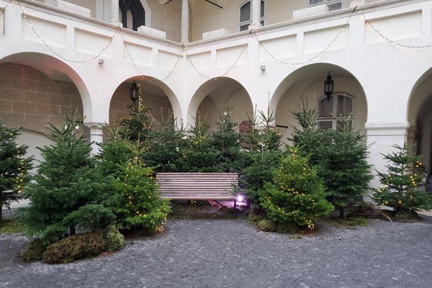 A courtyard with arched walkways, Christmas trees, and a bench. 5