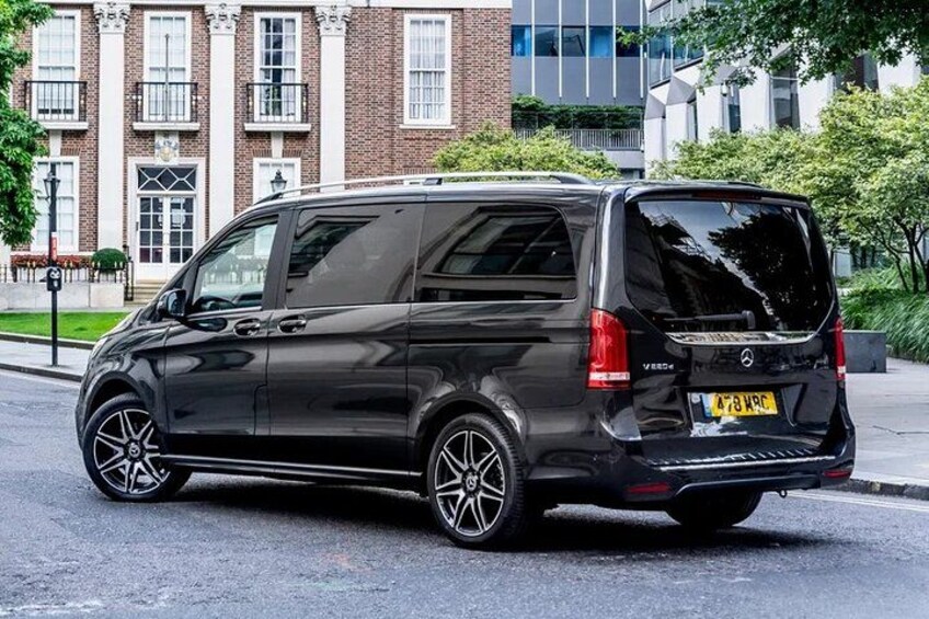A black van parked on a street with a brick building and modern architecture in the background. 2