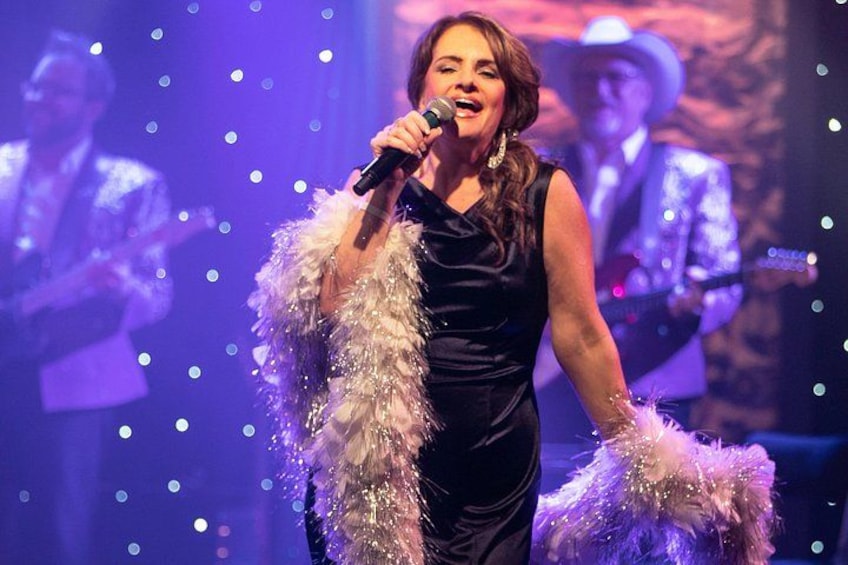A person on stage with a microphone, wearing a black dress and a feathered shawl. 2