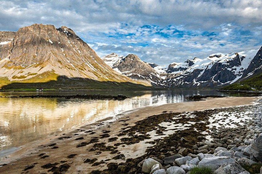 A mountainous landscape with a lake reflecting the mountains, a rocky shoreline, and snow-capped peaks. 2
