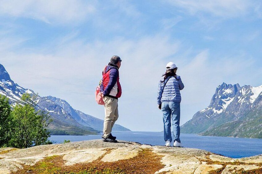 Zwei Personen stehen auf einer Felsformation und blicken auf einen See mit Bergen im Hintergrund. 1