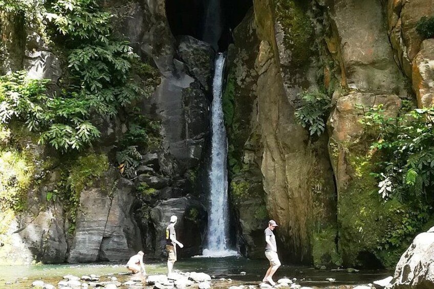 A waterfall, rocky cliffs, and a person standing in a shallow stream. 4