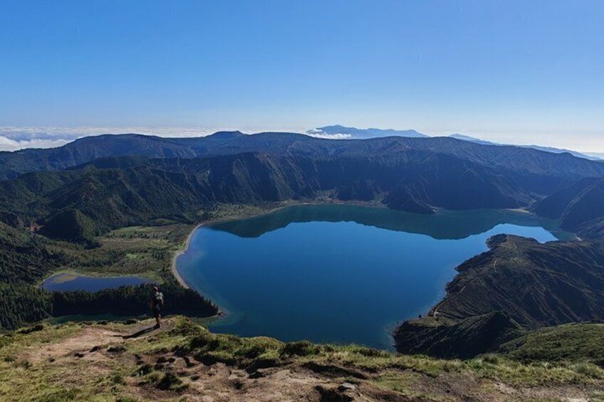 Un lac entouré de montagnes, une personne debout sur une colline et un ciel dégagé. 4