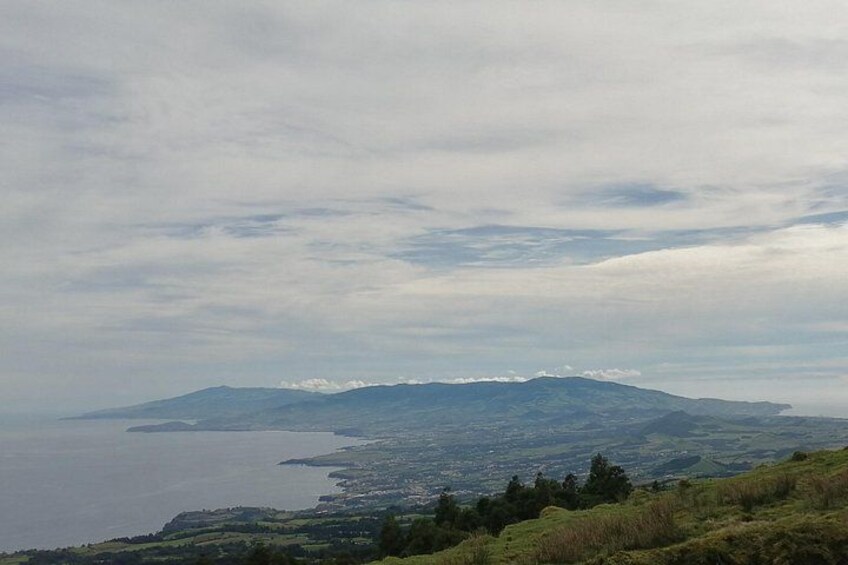 A coastal landscape with a mountain range in the distance, a body of water, and a hilly foreground. 5