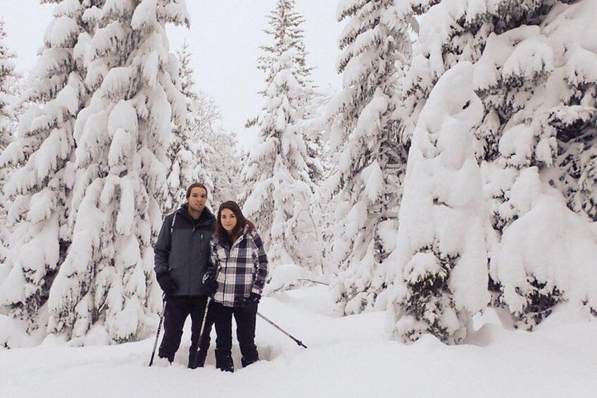 Twee personen staan in een besneeuwd bos met sneeuw bedekte bomen. 5