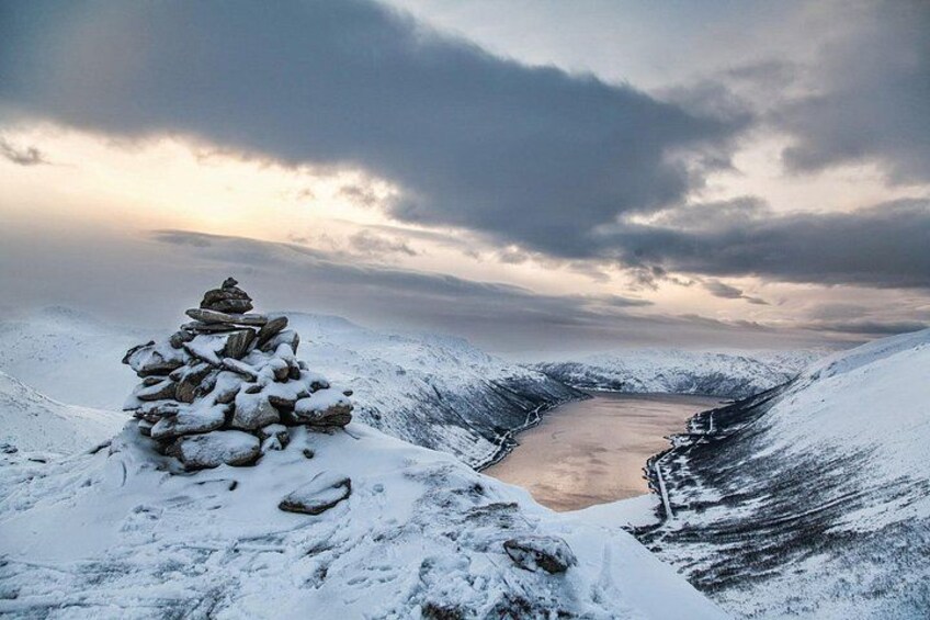 A snow-covered landscape with a cairn and a valley. 4