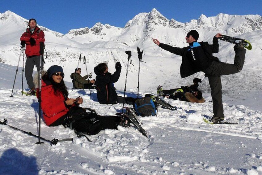 A group of people on a snowy mountain with ski equipment, some sitting and one standing with a ski board. 3