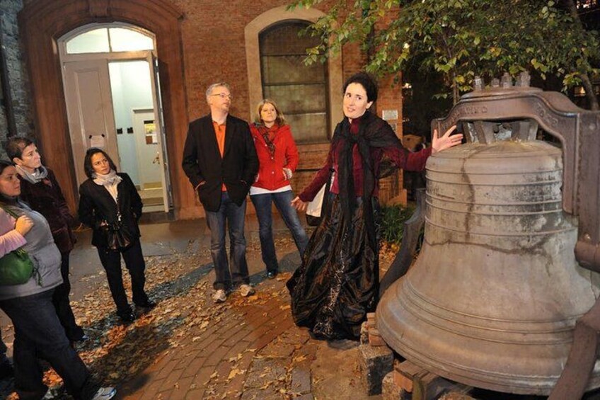 A group of people standing in front of a large, old-fashioned bell. 2
